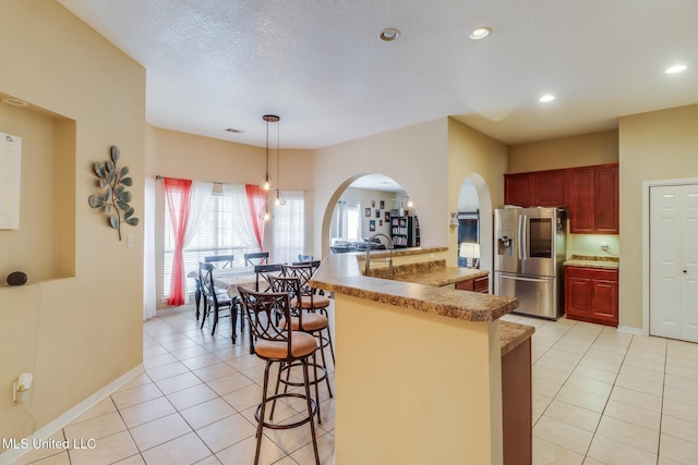 kitchen featuring reddish brown cabinets, stainless steel fridge, a breakfast bar, decorative light fixtures, and light tile patterned flooring