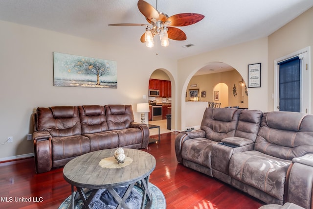 living area featuring arched walkways, a ceiling fan, visible vents, baseboards, and dark wood-style floors