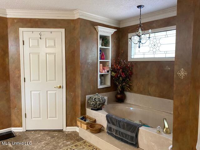 bathroom featuring a tub to relax in, a textured ceiling, an inviting chandelier, and ornamental molding