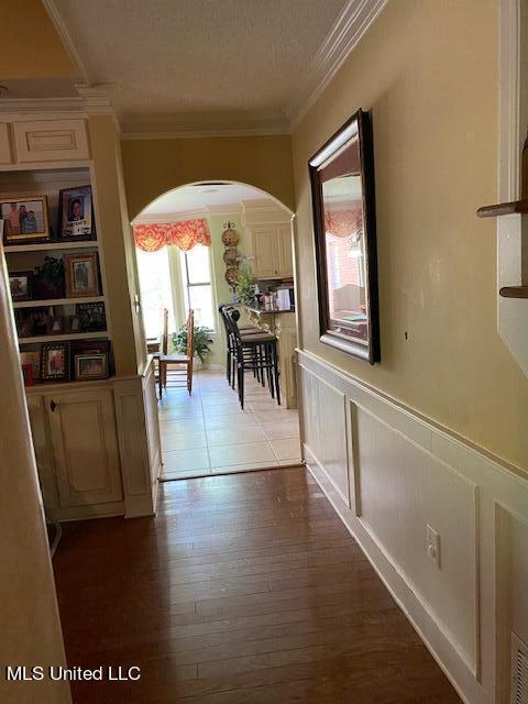 7235 Davidson Rd, Olive Branch, MS 38654 - hall featuring arched walkways, crown molding, a wainscoted wall, wood finished floors, and a decorative wall