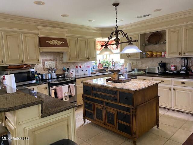 kitchen with appliances with stainless steel finishes, cream cabinetry, dark stone counters, and a kitchen island