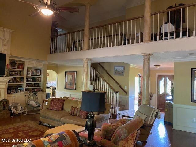 living room featuring ceiling fan, wood-type flooring, ornamental molding, ornate columns, and a towering ceiling