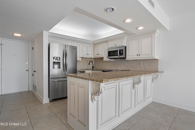 kitchen featuring appliances with stainless steel finishes, kitchen peninsula, tasteful backsplash, and a raised ceiling