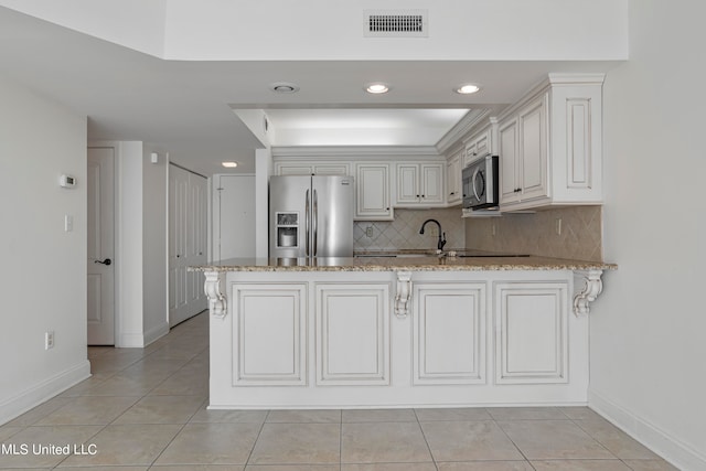 kitchen with kitchen peninsula, decorative backsplash, white cabinets, light stone counters, and stainless steel appliances