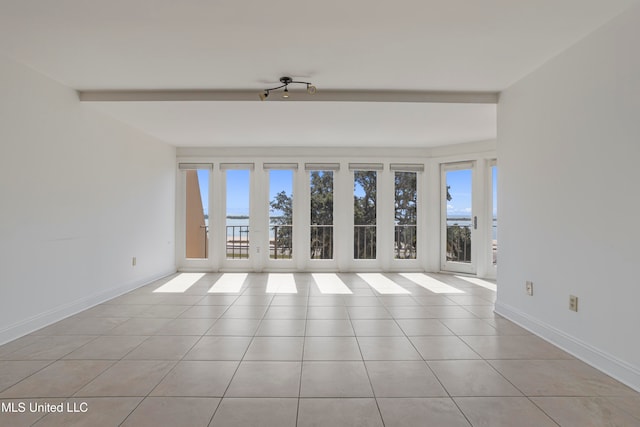 spare room with beamed ceiling, light tile patterned floors, and a wealth of natural light