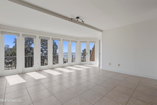 tiled spare room featuring vaulted ceiling with beams, a healthy amount of sunlight, and a water view