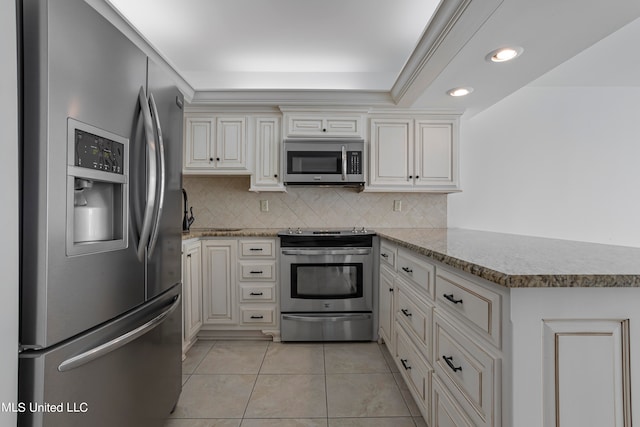 kitchen with cream cabinetry, backsplash, kitchen peninsula, stainless steel appliances, and light tile patterned floors