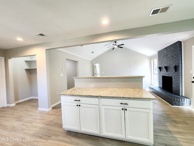 kitchen with visible vents, open floor plan, a center island, lofted ceiling, and a brick fireplace