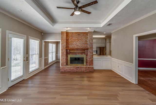 unfurnished living room with a textured ceiling, ornamental molding, a tray ceiling, a fireplace, and light hardwood / wood-style floors