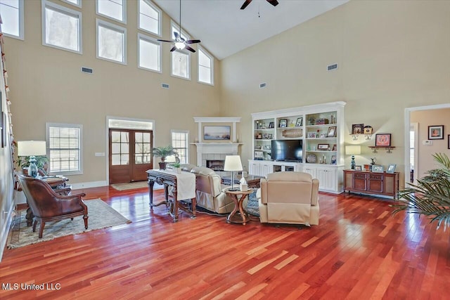 living room with a tile fireplace, wood-type flooring, and a high ceiling