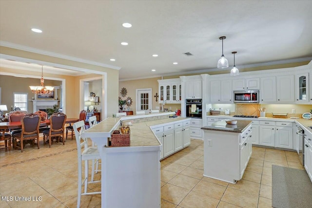 kitchen with a center island, a notable chandelier, pendant lighting, white cabinets, and appliances with stainless steel finishes