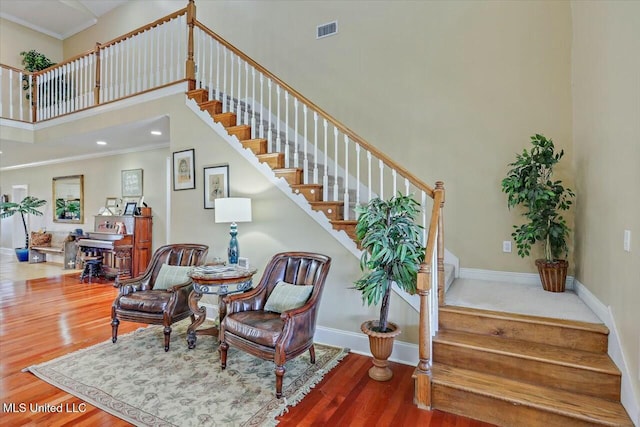 living area featuring crown molding, wood-type flooring, and a high ceiling