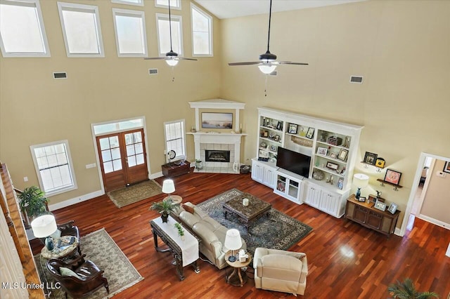 living room with ceiling fan, dark hardwood / wood-style flooring, a towering ceiling, and a fireplace