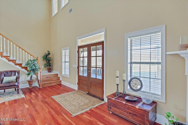 foyer entrance with french doors, a towering ceiling, and light hardwood / wood-style floors