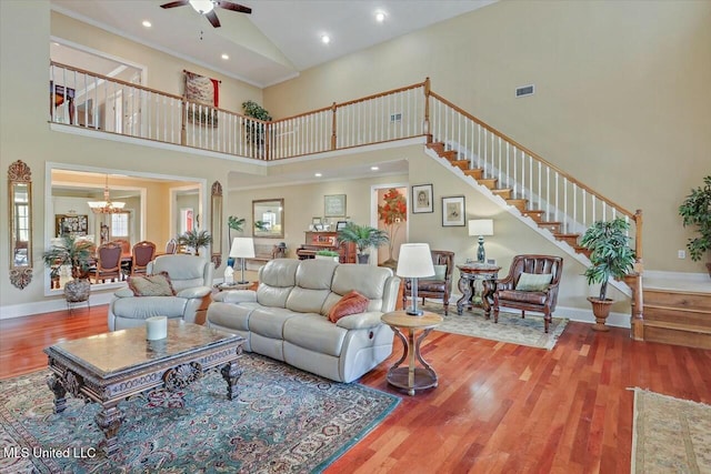 living room featuring ceiling fan with notable chandelier, wood-type flooring, and a high ceiling