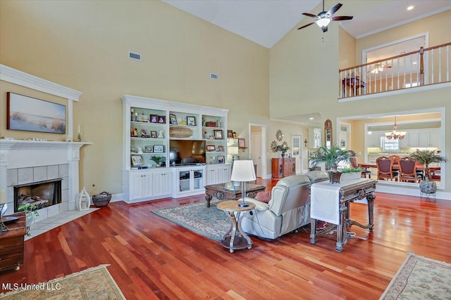 living room featuring ceiling fan with notable chandelier, a towering ceiling, hardwood / wood-style flooring, and a tiled fireplace