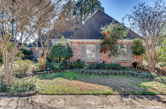 view of front facade featuring roof with shingles, a front yard, and brick siding