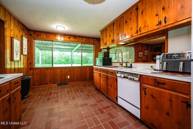 kitchen featuring white dishwasher, a sink, brick patterned floor, and wooden walls