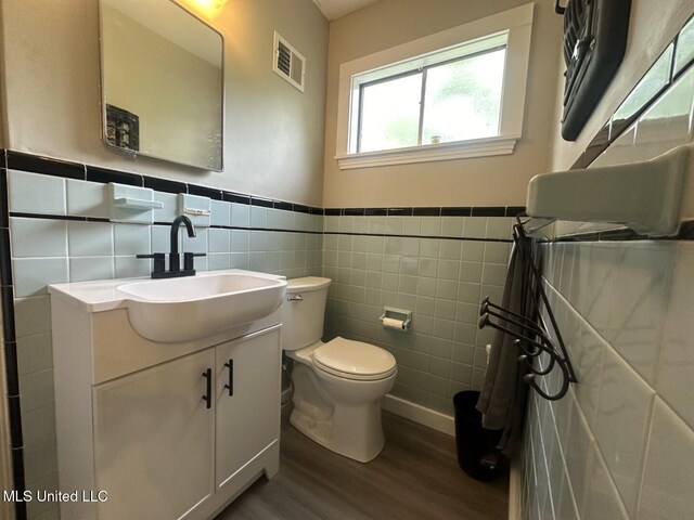 bathroom with visible vents, vanity, wood finished floors, toilet, and tile walls