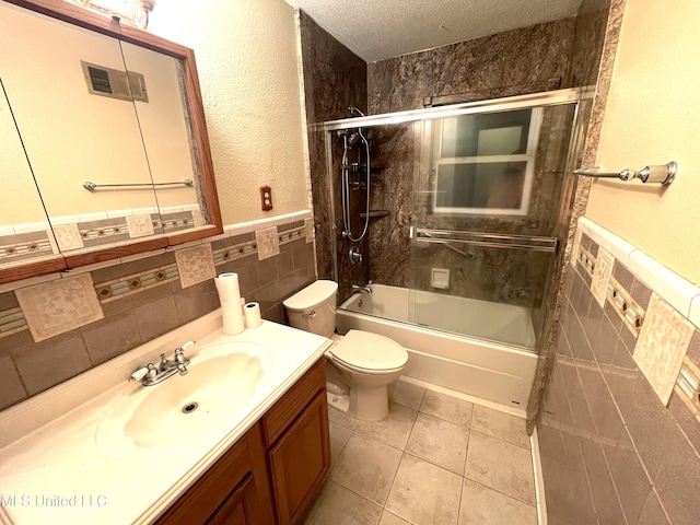 full bathroom featuring a textured ceiling, tile patterned flooring, tile walls, bath / shower combo with glass door, and vanity