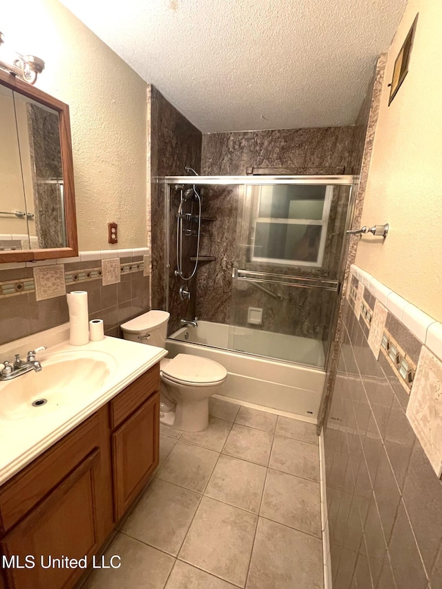 full bathroom featuring tile walls, combined bath / shower with glass door, a textured ceiling, and vanity