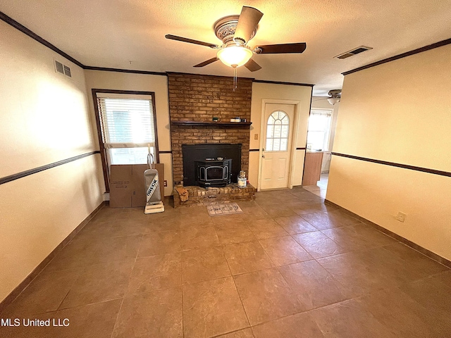 unfurnished living room featuring a textured ceiling, ceiling fan, a wood stove, and crown molding