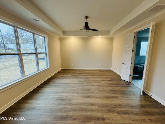 empty room with a tray ceiling, a ceiling fan, wood finished floors, and baseboards