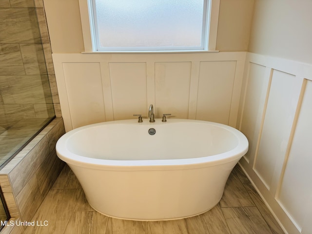 bathroom featuring healthy amount of natural light, a decorative wall, a freestanding bath, and wainscoting