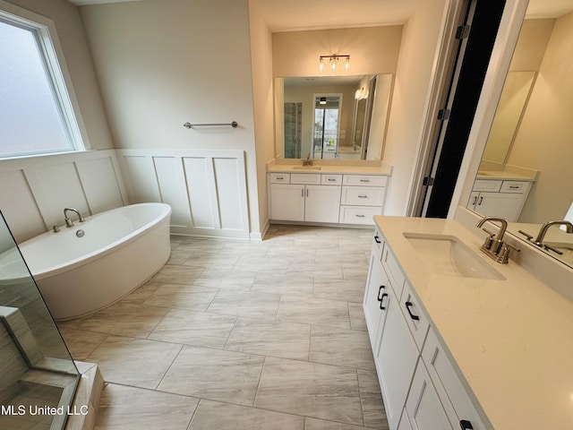 full bathroom with marble finish floors, a decorative wall, a soaking tub, two vanities, and a wainscoted wall