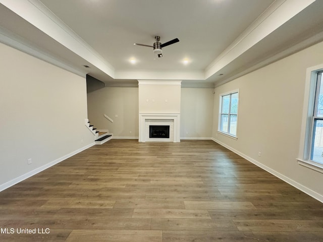 unfurnished living room featuring a raised ceiling, a ceiling fan, stairs, ornamental molding, and wood finished floors