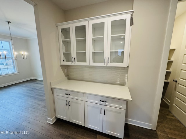 bar featuring decorative backsplash, a chandelier, baseboards, dark wood finished floors, and ornamental molding