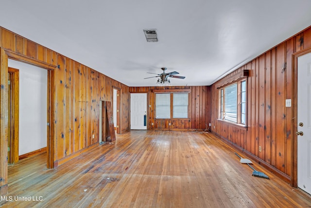 unfurnished living room featuring light wood-style flooring, baseboards, visible vents, wood walls, and ceiling fan