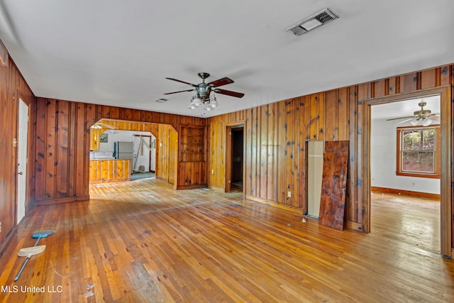 unfurnished living room featuring a ceiling fan, baseboards, wood-type flooring, wood walls, and visible vents