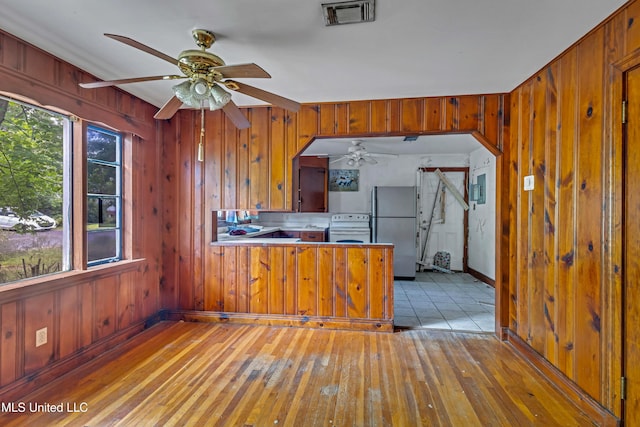 kitchen featuring freestanding refrigerator, visible vents, a ceiling fan, and wooden walls