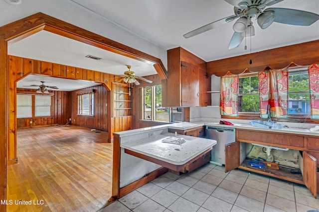 kitchen with a ceiling fan, a sink, dishwasher, wood walls, and visible vents