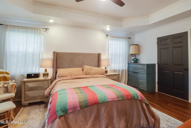 bedroom with ceiling fan, wood finished floors, ornamental molding, and a tray ceiling