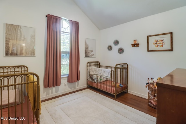 bedroom with a nursery area, lofted ceiling, multiple windows, and wood finished floors