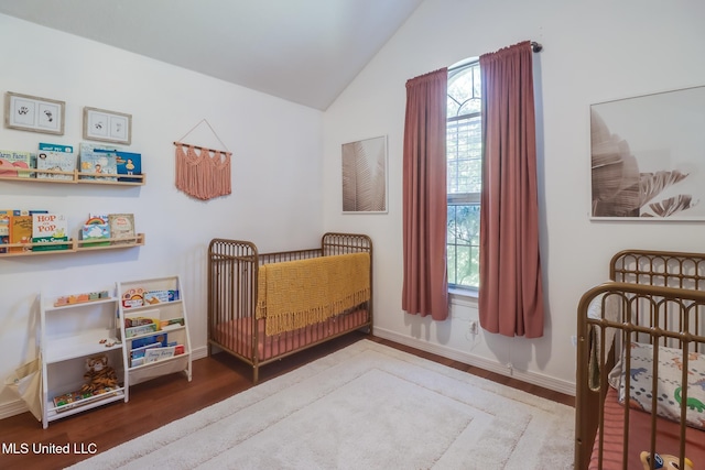 bedroom featuring a nursery area, wood finished floors, lofted ceiling, and baseboards