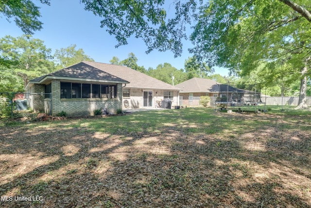 rear view of property featuring a lawn, a fenced backyard, brick siding, and a trampoline