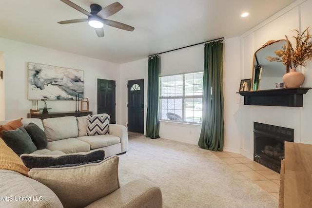 living area with a ceiling fan, light tile patterned floors, a fireplace with flush hearth, light colored carpet, and baseboards