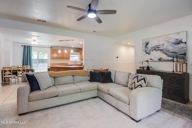living area featuring wainscoting, light carpet, visible vents, and ceiling fan