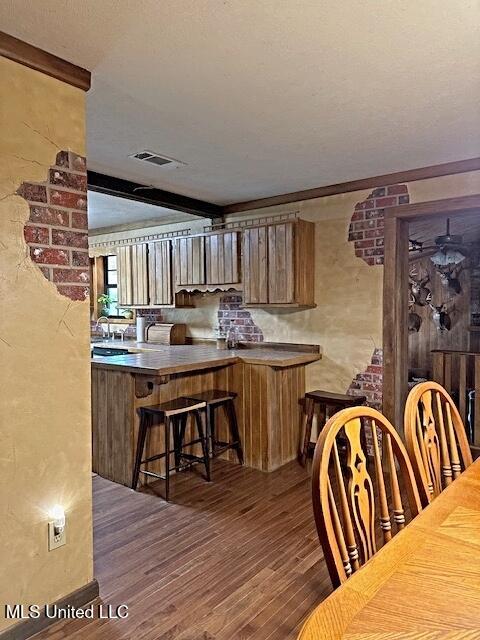interior space with a textured ceiling, visible vents, brown cabinets, a kitchen bar, and wood finished floors