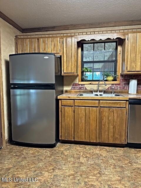 kitchen with a textured ceiling, crown molding, brown cabinets, stainless steel appliances, and a sink