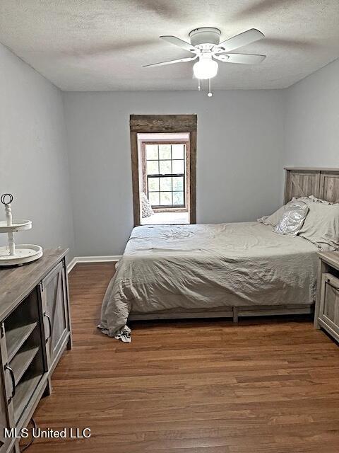 bedroom with a ceiling fan, baseboards, a textured ceiling, and dark wood finished floors