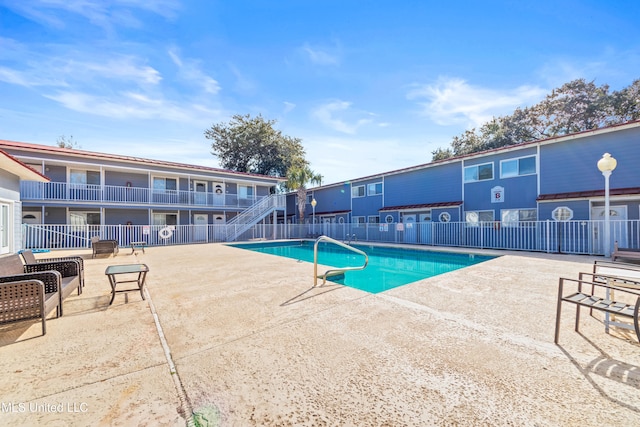 community pool with stairway, fence, and a patio area
