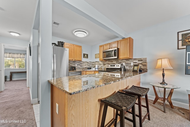 kitchen featuring appliances with stainless steel finishes, light colored carpet, stone countertops, light brown cabinetry, and a peninsula