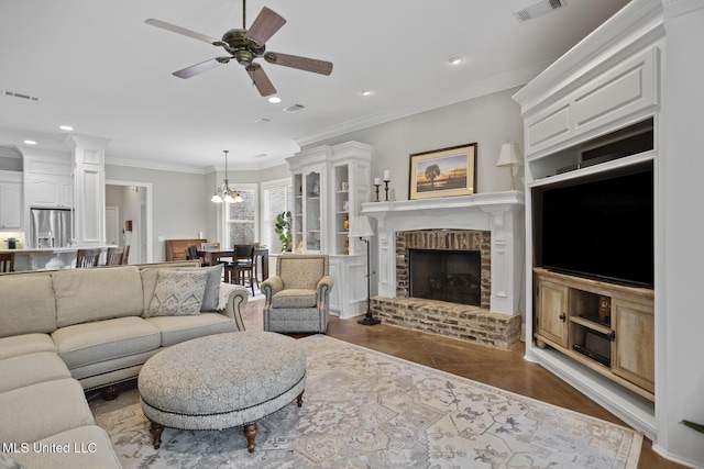 living room featuring ceiling fan with notable chandelier, a brick fireplace, visible vents, and ornamental molding