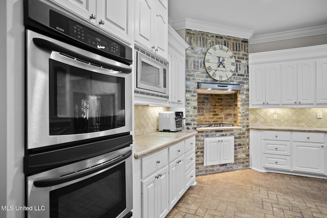 kitchen with ornamental molding, appliances with stainless steel finishes, white cabinetry, and brick floor