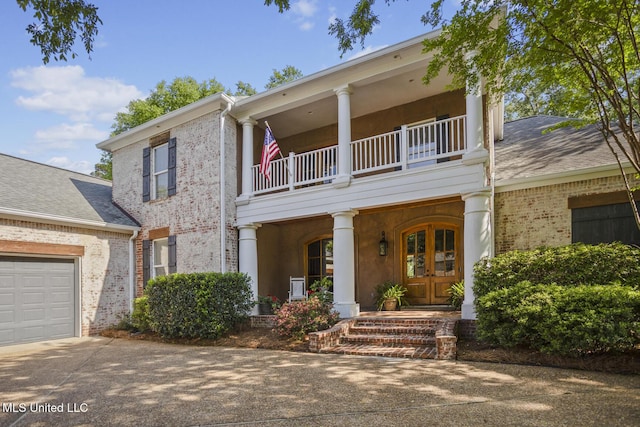 view of front of house featuring brick siding, driveway, a balcony, and french doors