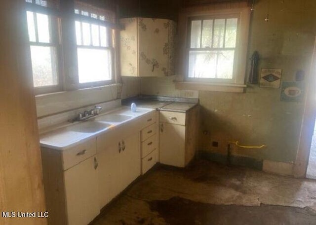 kitchen with light countertops, a sink, white cabinetry, and a healthy amount of sunlight